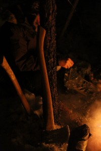 An axe proped up against a tree, as the prior users gather around the fire at their finished camp at Duck Lake in Yellowknife, NWT.